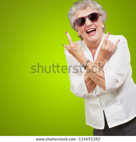 Senior woman wearing sunglasses doing funky action isolated on green background