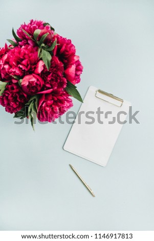Clipboard and pink peonies flowers bouquet on pastel blue background. Flat lay, top view workspace mock up.