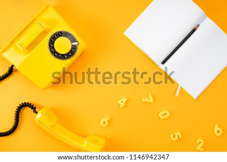 top view of vintage phone with blank notebook and numbers on yellow