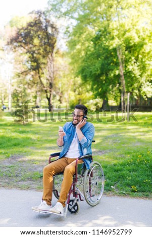 Modern young handicapped man in a wheelchair listening music outdoor