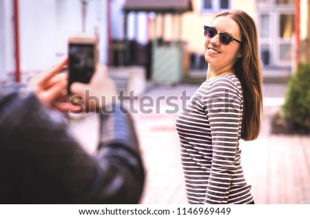 Man taking photo of his female friend. Happy lady posing for smartphone camera in city street. Young woman smiling. Tourists taking pictures. Travel, tourism and mobile photography concept.