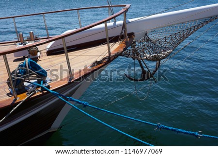 Bow of a black sailing yacht against the blue sea with anchor at the bow. 