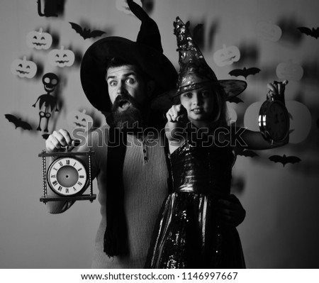 Girl and bearded man with scared and confident faces on pink background. Wizard and little witch in black hats hold old clocks. Halloween party and celebration concept. Father and daughter in costumes