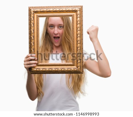 Blonde teenager woman holding vintage frame art annoyed and frustrated shouting with anger, crazy and yelling with raised hand, anger concept