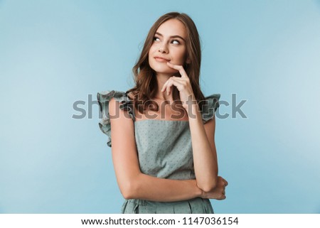 Picture of pretty young lady standing isolated over blue background looking aside.
