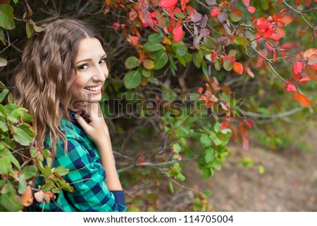 Elegant young girl with beautiful hair posing in beautiful autumn wood on a background of yellow leaves. Early autumn.