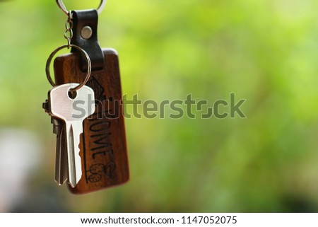 House keys with wooden home keyring with blur green garden background, property concept, copy space