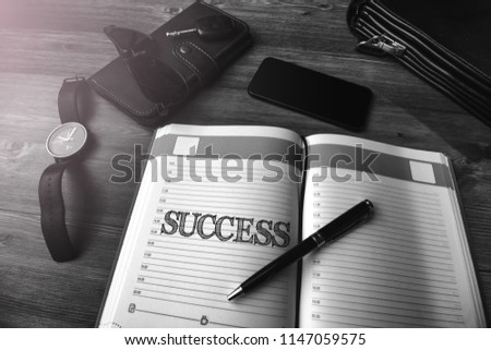 Men's accessories (bag, keys, purse, notebook and glasses) on a wooden table with text Success
