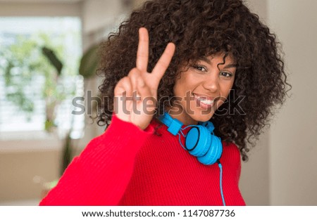 African american woman wearing headphones smiling looking to the camera showing fingers doing victory sign. Number two.