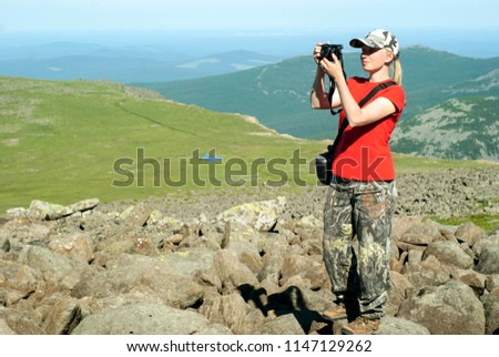 girl photographer hiker takes a picture standing on a high mountainside in the background of a mountain landscape