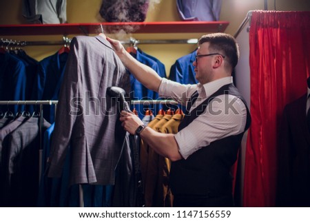 tailor cuts and sews a suit. A young man in the tailoring shop makes men's clothing. Custom-made clothing workshop. holds in her hand an electric iron. wet-heat treatment