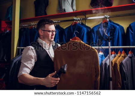 tailor cuts and sews a suit. A young man in the tailoring shop makes men's clothing. Custom-made clothing workshop. holds in her hand an electric iron. wet-heat treatment