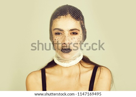 woman with black lips, makeup, wearing white, fishnet stocking on head and face as robber or gangster with long, brunette hair on grey background. Crime, criminal