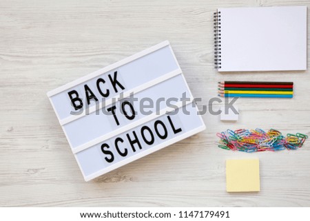 'Back to school' word on lightbox, accessories for study over white wooden background, overhead view. Top view, flat lay, from above.