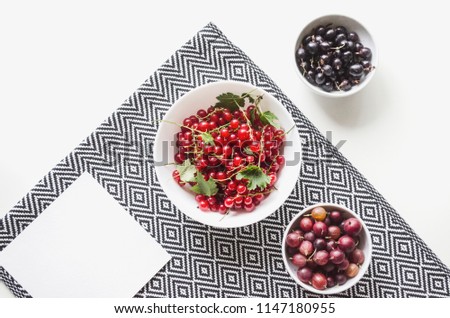 Fresh red currants and gooseberries in a plate on a table with a graphic napkin. Flat lay, top view, copy space,  mock-up