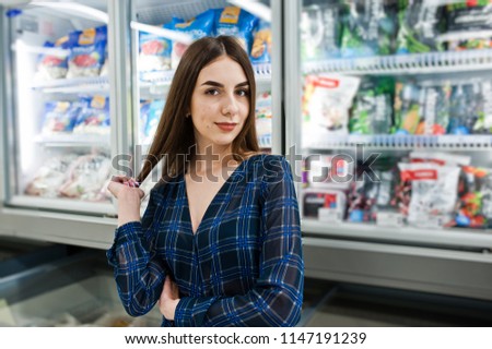 Shopping woman looking at the shelves in the supermarket.  Portrait of a young girl in a market store taking seafood from fridge.