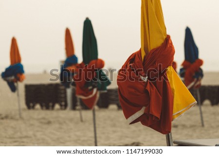 Beach umbrellas on foggy morning in Deauville, fashionable holiday resort in Normandy, France. Folded colorful parasols and lounge chairs on the empty beach. Leisure and seaside vacations concept