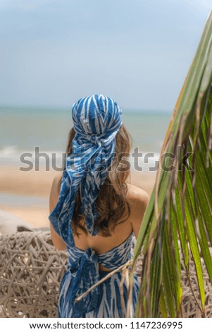 Young woman in summer dress standing by blue sea and looking to horizon