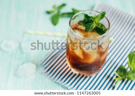 The glass of peach ice tea on wooden table. Cuba Libre or long island iced tea cocktail, cold drink or lemonade with fruits and mint