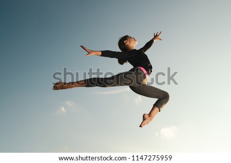 Smiling, happy young girl gymnast acrobat jumping high in the sky. Royalty-Free Stock Photo #1147275959