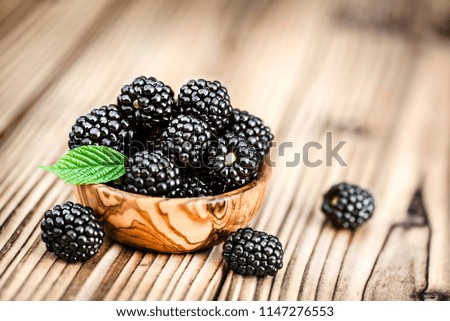 Black berry on rustic or old wooden table. Forest fruits like blackberries in olive bowl.