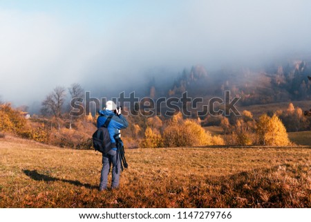 Photographer taking photo of autumn landscape with foggy peaks and orange trees. Ukrainian Carpathians mountains