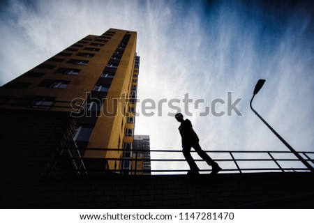 Teenage boy on a street in a big city next to a high-rise building alone. concept of a teenager parkour life. portrait on a high wall silhouette close view