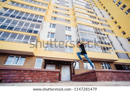 Teenage boy on a street in a big city next to a high-rise building alone. concept of a teenager parkour life. parkour jump on a high-rise building background from the side