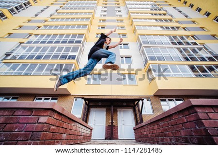 Teenage boy on a street in a big city next to a high-rise building alone. concept of a teenager parkour life. parkour jump on a high-rise building background from the side close up view