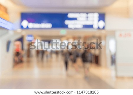 Blurred background passengers or tourist walking at airport hallway with Illuminated direction sign. Motion blurry people walk away with luggage at American terminal. Travel and transportation concept