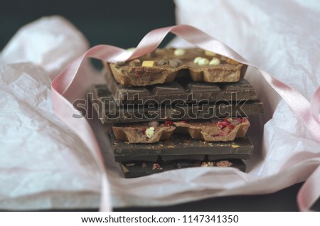 A gift pack of artisan handmade chocolate. Chocolate bars with dried fruit in pink tissue paper on dark background.