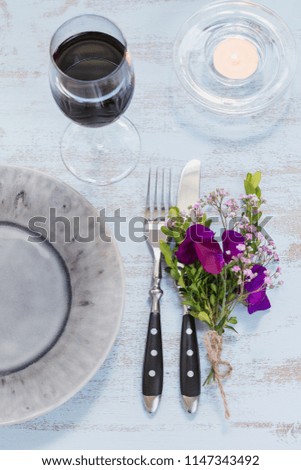 Rustic table setting with purple flowers, candle and a glass of red wine on light wooden table. Holidays decoration on Provence style. Romantic dinner. Top view 