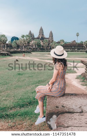 Young female tourist wearing a hat with backpack is posing at Angkor Wat temple, Siem Reap, Cambodia
