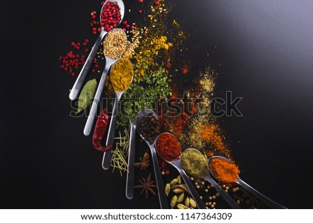 Composition of small spoons full of spices and condiments for cooking on a black background