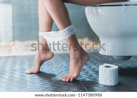 Beautiful Slender Legs of Girl on Toilet with Downed Panties. Woman on Toilet. Next Roll of Toilet Paper. Diarea and Digestive Problems. Hygiene Concept. White Lavatory and Bathroom.