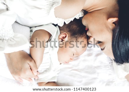 Mother kiss and holding sleeping baby hand on white bed.Love of family concept