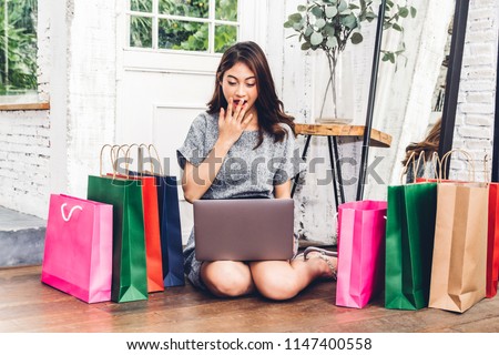Beautiful woman shoping online with technology of laptop computer and colorful shopping bag sitting on the floor at home Royalty-Free Stock Photo #1147400558