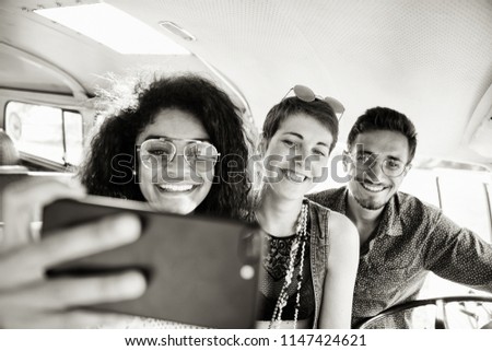Mixed group of happy young people in a vintage van having fun doing a selfie with a phone. They look hipster and going vacation. black and white