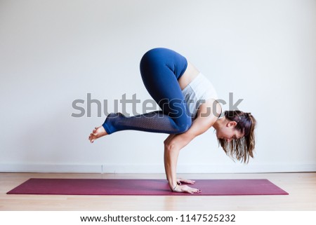 Portrait of young yogi woman practising yoga, wearing blue sportswear, white studio background, crow pose (selective focus)