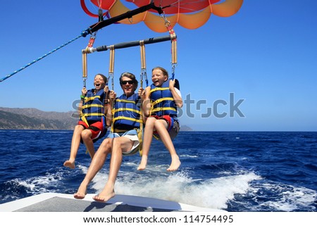 Father and Twin Daughters Parasailing Against a Blue Summer Sky. Royalty-Free Stock Photo #114754495