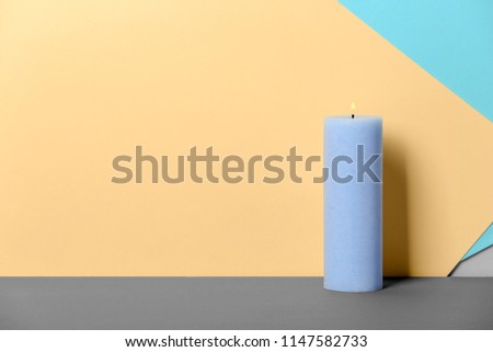 Decorative wax candle on table against color background