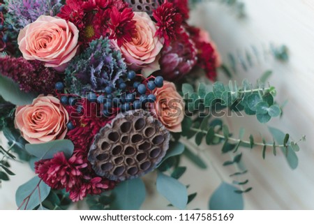 Bouquet of autumn flowers in red, burgundy and shades of Marsala. Ingredients: protea, roses, berries, eucalyptus, cotton flower, lotus flower, chrysanthemum, ornamental cabbage. Flower composition.