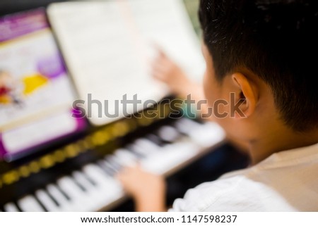 Blurry picture of woman teaching boy to play the piano with selective focus. Four hands from two people playing piano with music notation. There are musical instrument for learning music.