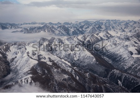 View of the mountains covered with snow from the airplane. Mountains to horizon. Mountain range in cloudy weather