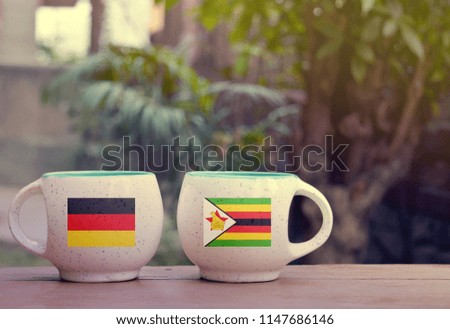 Germany and Zimbabwe Flag on two tea cups with blurry background