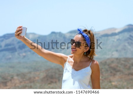 Beautiful woman doing a selfie on top of a mountain, with beautiful views of the vicinity of the teide behind her, looking fixedly at the mobil.