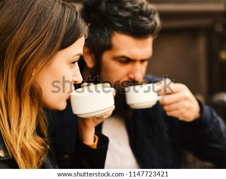 Girl and bearded guy have coffee on brown terrace background. Couple in love drinks espresso during coffee break. Dating at urban cafeteria concept. Woman and man with serious faces have date at cafe. Royalty-Free Stock Photo #1147723421