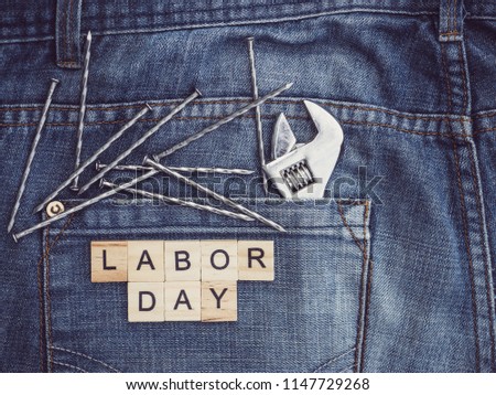 Tools and wooden letters with the inscription LABOR DAY on the background of a blue jeans pocket. Top view, close-up. Preparation for the celebration of Labor Day