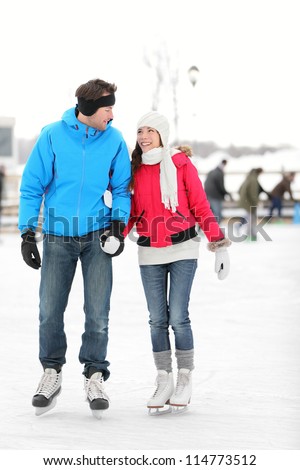 Romantic young couple in warm winter clothing holding hands and smiling at each other while ice skating.