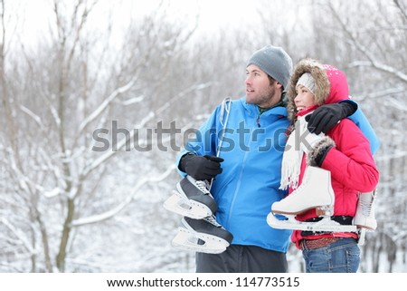 Young interracial couple in winter carrying ice skates standing close together looking out over a snowy winter landscape with copyspace. Asian woman, Caucasian man.